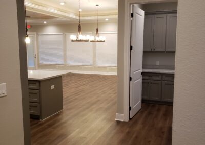 view of side of kitchen island from the walkway behind with living room in the distance and a view of the laundry room with partially opened door revealing gray storage cabinets