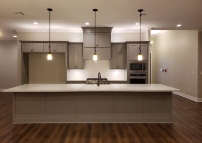 view of kitchen head on from living room with long gray and white quartz island below three hanging pendants with microwave and oven and stove on back wall