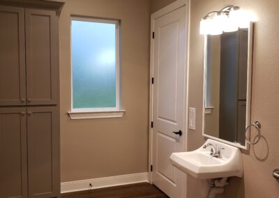 side view of wheelchair accessible sink with mirror and three bulb light fixture with beige walls and gray storage cabinetry