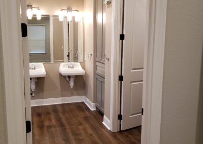 view of double sink wheelchair accessible sinks with mirrors and light fixtures with built-in bathroom storage cabinetry and door opening to shower room