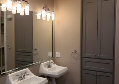 side view of double wheelchair accessible wall mounted sinks with mirror and light fixtures on beige walls and built-in bathroom storage cabinets