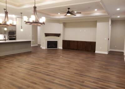wide view of empty living room and kitchen open layout medium brown wood flooring with cream walls and dark wood fireplace mantel