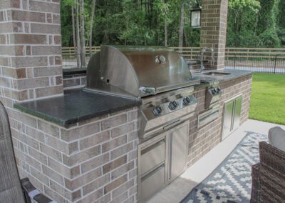 light brock with black countertops outdoor kitchen with stainless steel grill, sink, and storage drawers