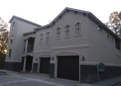tan stucco house with dark brown details and black light fixtures with a dark brown stone strip along the bottom of the home