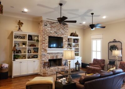 living room with tan walls and white trim with a light red brick floor to ceiling fireplace encased between white built-in shelving