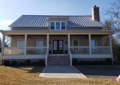 front exterior view of a pier and beam house with a long front porch with white railing and light red brick staircase