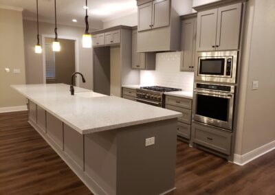 diagonal view of kitchen with white tiling above stove and stainless steel appliances plus a large gray island with white quartz countertops