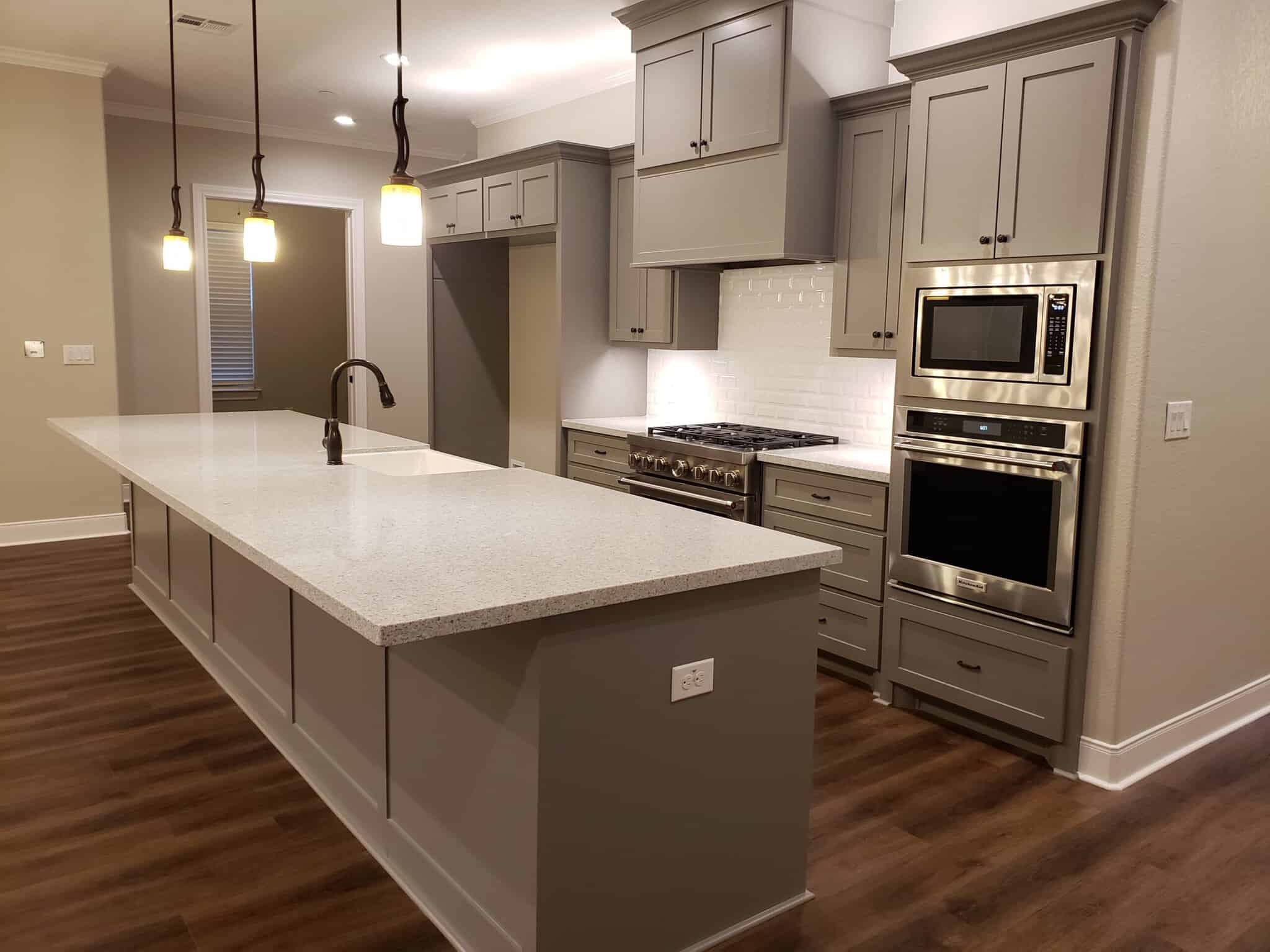 Dreams 2 Reality Customer Homes - Afzal Home Kitchen diagonal view of kitchen with white tiling above stove and stainless steel appliances plus a large gray island with white quartz countertops
