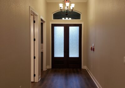 inside view of brown double entry doors with semi-transparent windows and an arched window above the door among beige walls with white trim and brown wood flooring