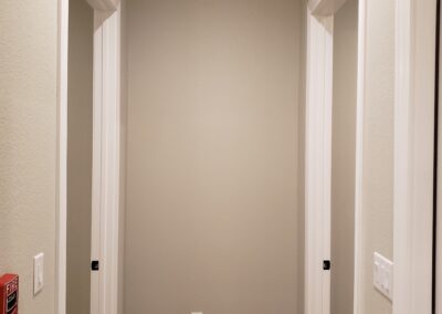 hallway view of two room entryways with open doors across from the other with beige walls and white trim