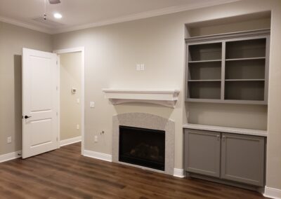 room with light beige walls and fireplace centered between open doorway and built-in cabinetry and shelving serving as a small entertainment and storage area