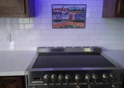 stainless steel stove with a white subway tile backsplash that has a small rectangular piece of artwork set into it