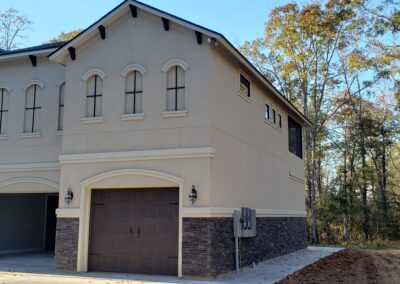 tan stucco house with dark brown garage door and 6 faux windows above it featuring a dark brown strip of stone around the bottom of the wall