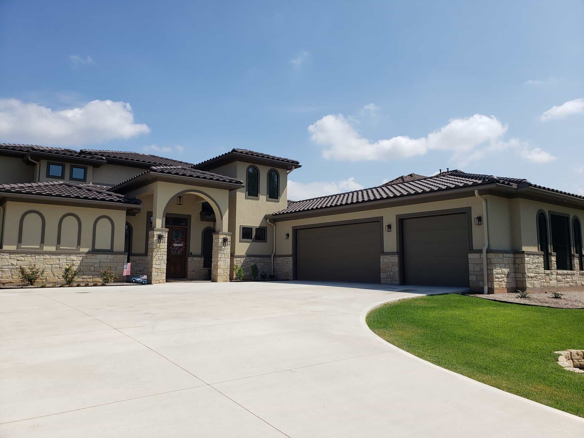 Dreams 2 Reality Custom Homes - Snyder Home Front Exterior front of a house with tan stucco and dark brown details with two dark brown garage doors and an arched front entry